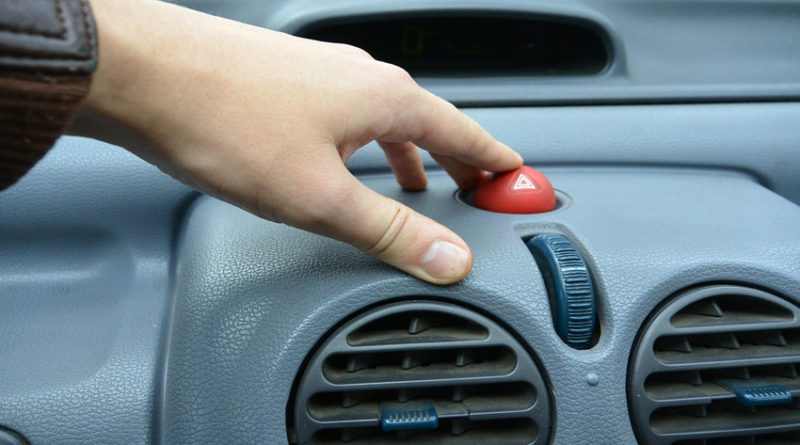 Finger pressing red hazard switch on car dashboard